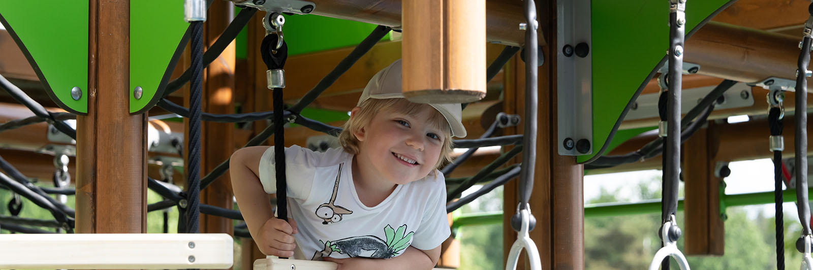 A young boy is peeking through a playground play system and smiling.